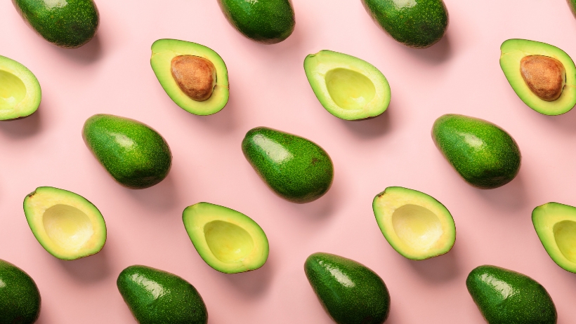Ein Muster aus ganzen und halbierten Avocados mit und ohne Kern ist auf einem rosa Hintergrund angeordnet und unterstreicht den Reiz der veganen Ernährung für Gesundheit.
